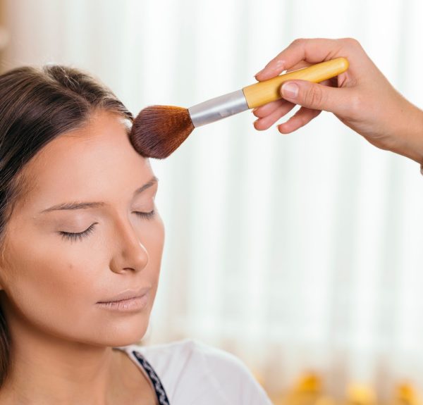 Make up artist working in a make up studio, applying the highlighters to female client's face